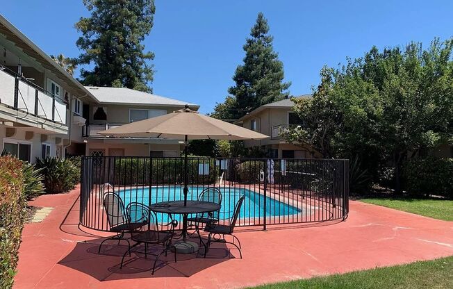 a swimming pool with a table and chairs behind a wrought iron fence