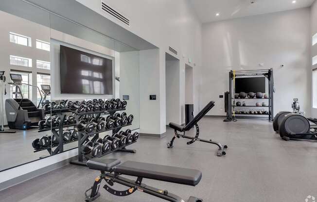 A spacious gym with a variety of equipment including dumbbells, weight plates, and a bench press.