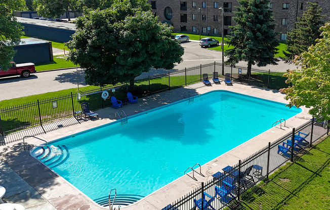A small pool surrounded by a black fence with blue chairs around it.