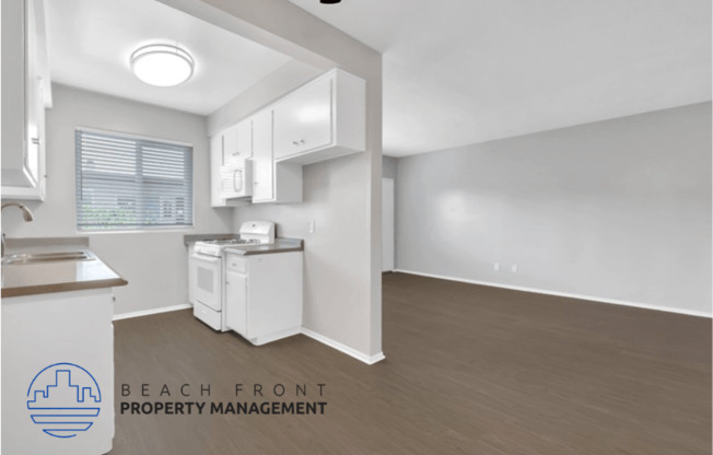 an empty living room and kitchen with white cabinets and wood flooring