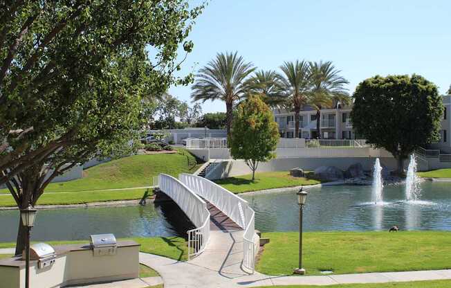 A park with a bridge over a pond and a fountain.