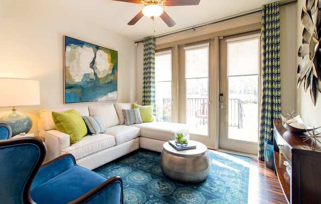 A living room with a white couch, blue chairs, and a painting on the wall.