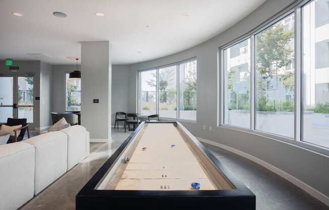 a shuffleboard table in the center of a living room with large windows