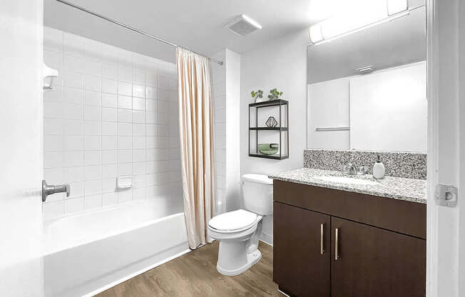A white toilet sits in a bathroom with a white tub and wooden floors.