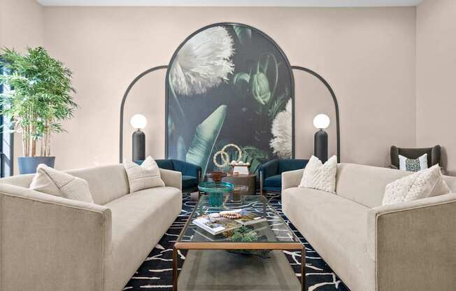 A living room with two beige couches, a glass coffee table, and a large mural on the wall.