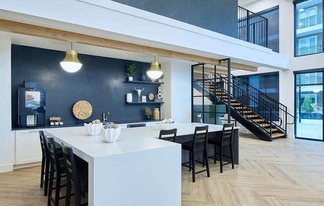 A modern kitchen with a white island and black chairs.
