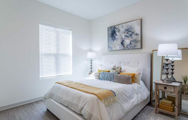 A bedroom with a white bed and a painting above it.