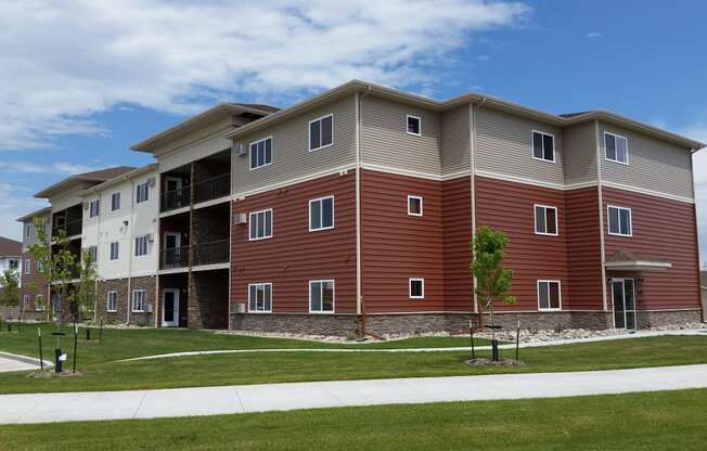 an exterior view of an apartment building with grass and a sidewalk. Fargo, ND Urban Plains Apartments