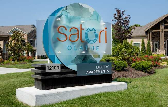 A sign for Satori Olai Luxury Apartments is displayed in front of some houses.