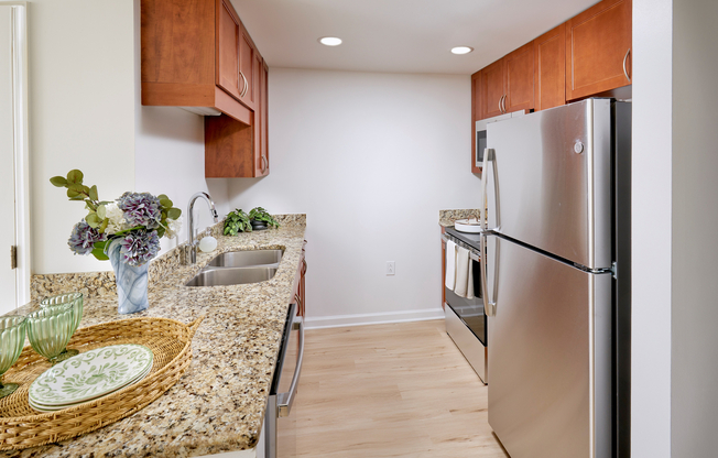 This modern studio kitchen features sleek stainless steel appliances that contrast beautifully with existing granite countertops and custom cabinetry. The space is tied together with new, durable vinyl plank wood-style flooring and updated overhead lighting.