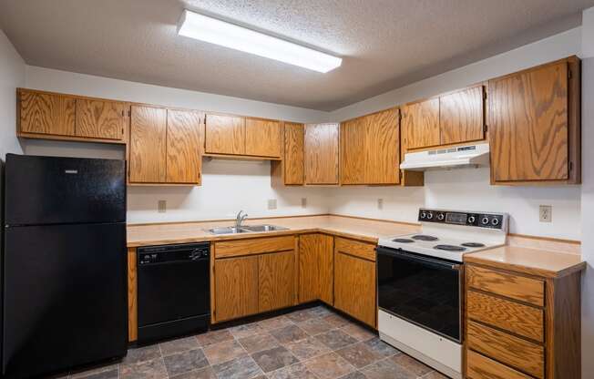 an empty kitchen with wooden cabinets and black appliances. Fargo, ND Southview Village Apartments