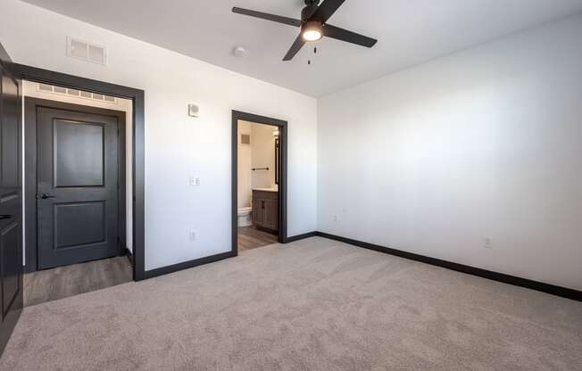 an empty living room with a ceiling fan and a door to a bathroom