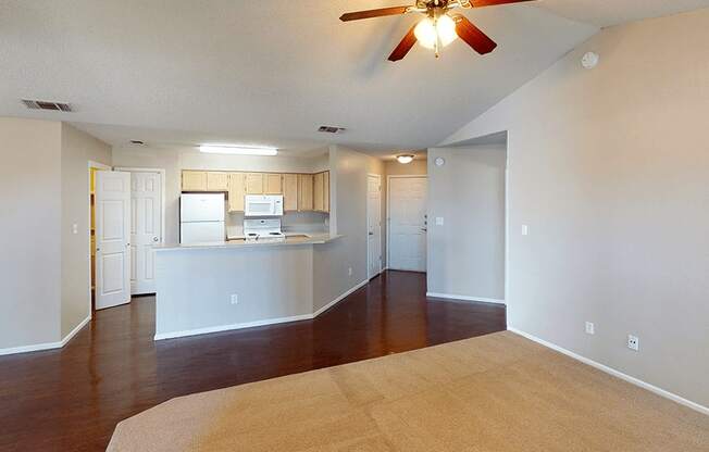 a living room with a ceiling fan and a kitchen in the background