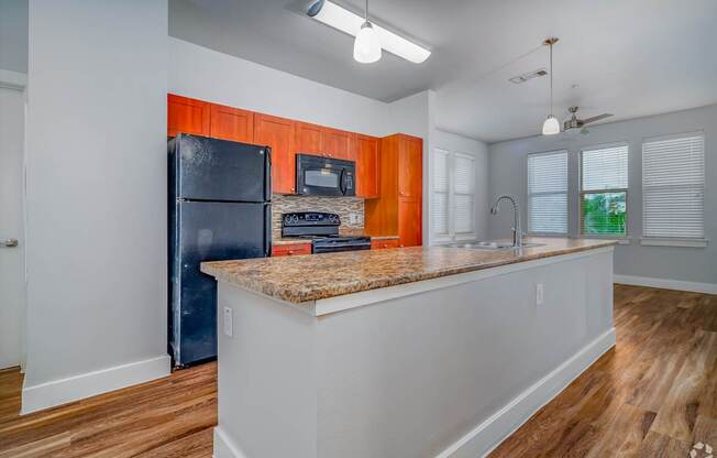 A kitchen with a black refrigerator and orange cabinets.