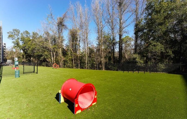 a red trash can sitting on top of a lush green field  at Fusion, Jacksonville, FL, 32256