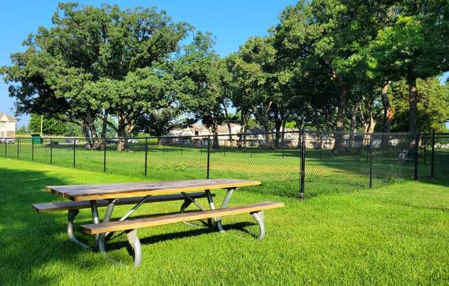 a picnic table in a grassy field with a chain link fence in the background at Beacon Hill and Great Oaks Apartments, Illinois