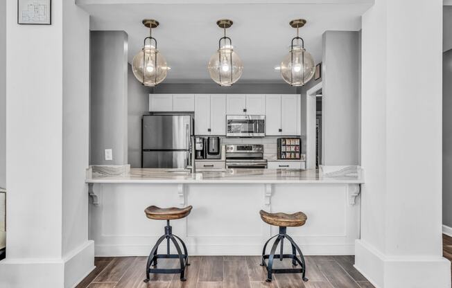 a kitchen with white cabinets and a bar with two stools