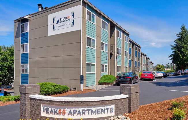 Community entrance with orange and gray 'Peak 88' sign surrounded by flowers and landscaping.