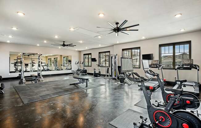 a spacious fitness room with cardio equipment and windows