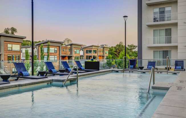 a swimming pool with blue lounge chairs and buildings in the background