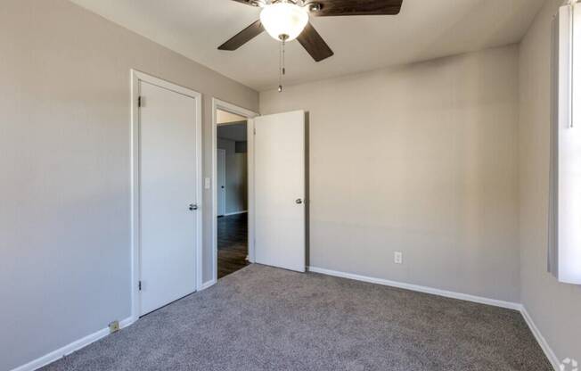 an empty living room with a ceiling fan and a door to a hallway