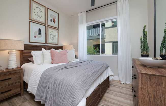 A bedroom with a bed, nightstand, and a window with white curtains.