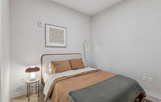 A bedroom with a bed, a lamp, and a picture on the wall.