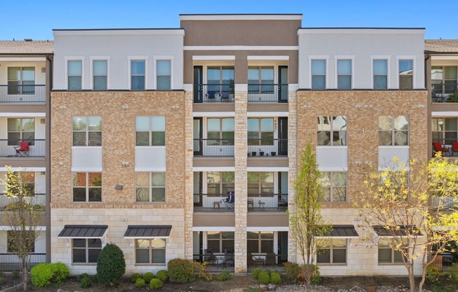 A row of apartment buildings with balconies and trees in front.