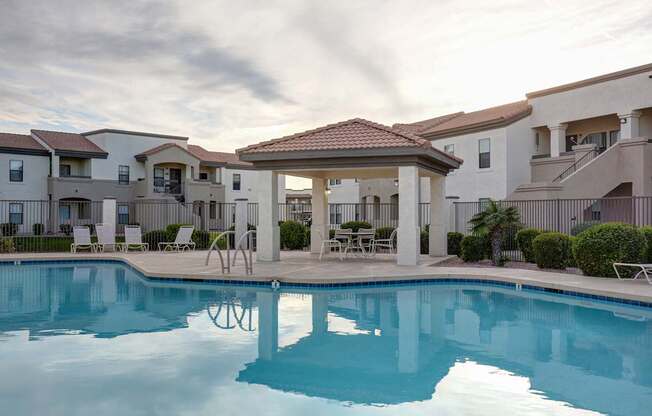 A swimming pool in front of a building with a gazebo.