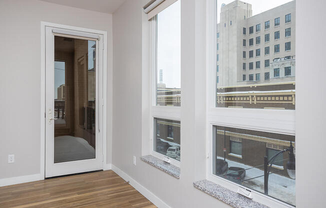a bedroom with three large windows and a door that leads to a balcony