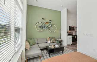 A living room with a grey couch and a bicycle on the wall at Link Apartments® CYKEL Apartments, North Carolina
