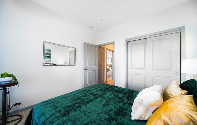 A bedroom with a green bedspread and a white dog on the bed.