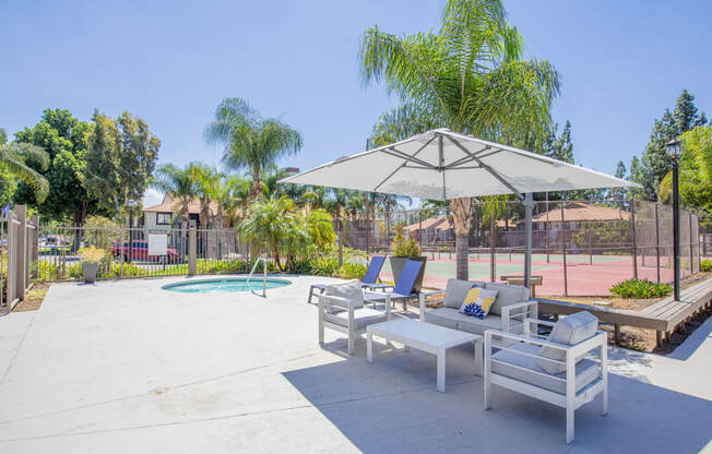a patio with two lounge chairs and an umbrella with a pool in the background