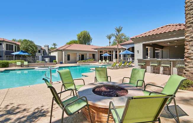 A poolside area with a fire pit and chairs.