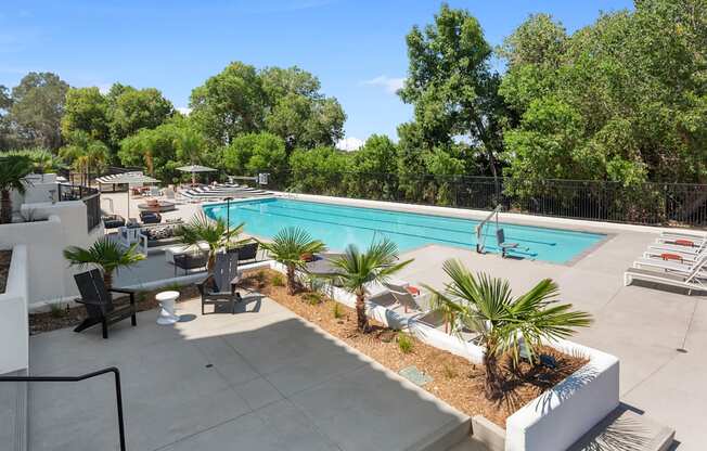 a swimming pool with tables and chairs and trees in the background