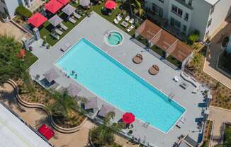 An aerial view of a swimming pool surrounded by red umbrellas and lounge chairs.