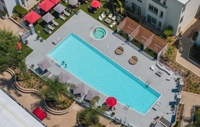 An aerial view of a swimming pool surrounded by red umbrellas and lounge chairs.