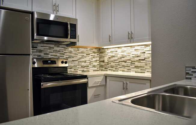 Kitchen with stainless appliances, tiled backsplash, and white cabinets