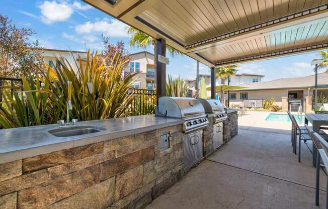 an outdoor kitchen with a barbecue and a pool in the background