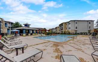 A pool area with sun loungers and a small building in the background.