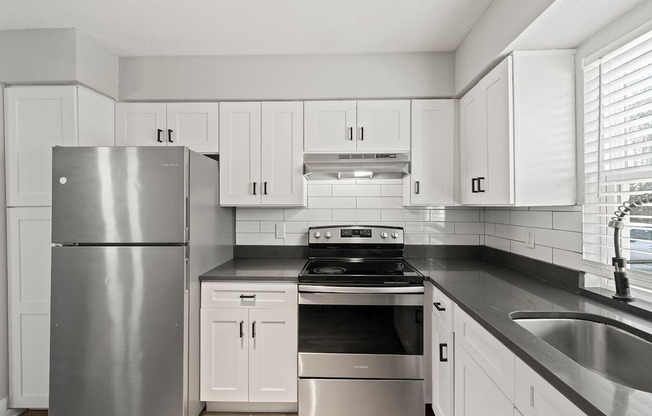 A modern kitchen with a stainless steel refrigerator, stove, and white cabinets.