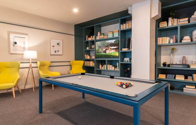 A pool table in a room with a yellow chair and a bookshelf.