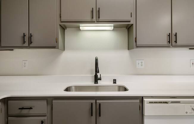 A kitchen with white countertops, a stainless steel sink, gray cabinets and a dishwasher.at Shoreline Village, Richland