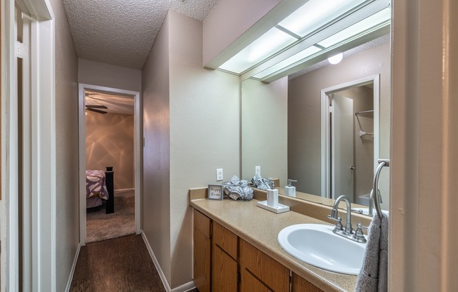 A bathroom with a sink, mirror, and a bed in the background.