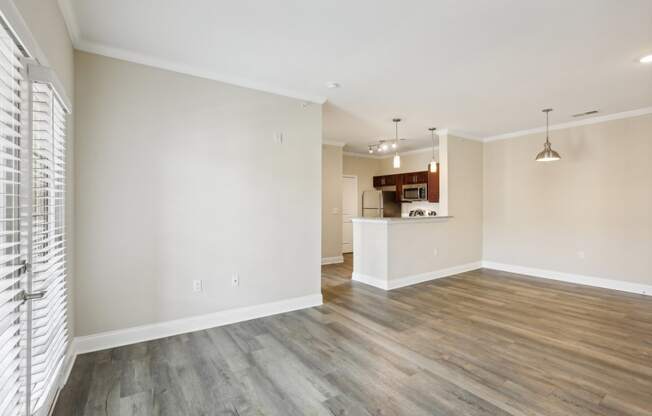 an empty living room with wood flooring and a kitchen