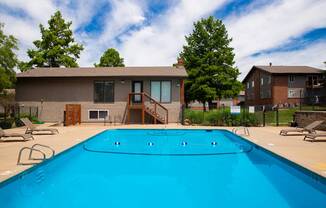 A swimming pool in front of a house with a deck and trees.