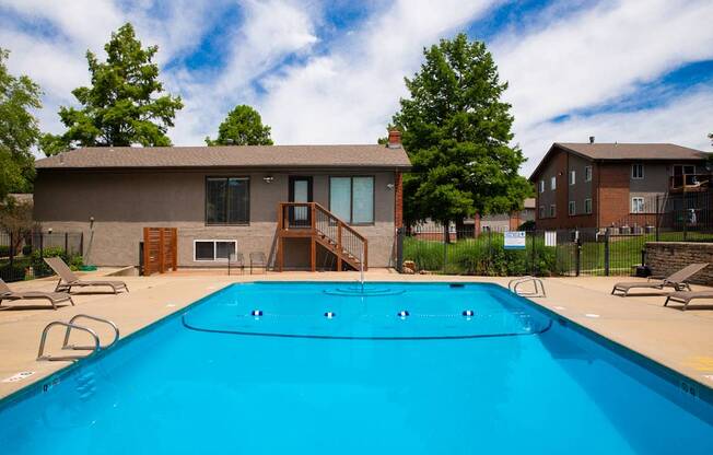 A swimming pool in front of a house with a deck and trees.