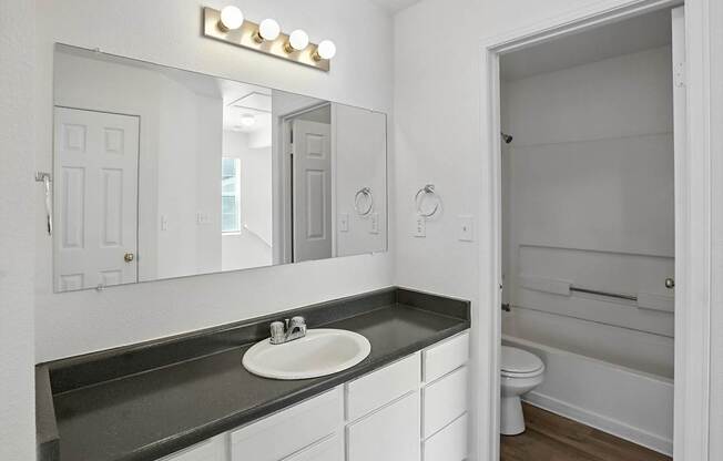 A bathroom with a sink, mirror, and toilet. at Oakstone Apartments, Clearfield, Utah