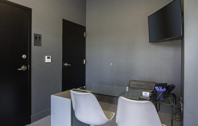 A black door is on the left of a room with a glass table and two white chairs.