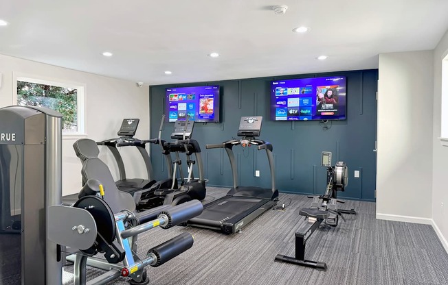 a gym with exercise machines and two televisions on the wall